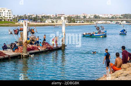 Les enfants nagent sur la jetée de la baie avec des bateaux de pêche et des filets dans le centre de Rabat, au Maroc Banque D'Images