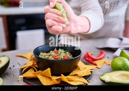Trempez la guacamole avec des chips de tortilla ou des nachos sur le plateau de service noir Banque D'Images