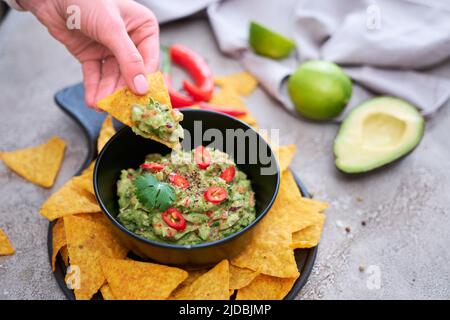 Trempez la guacamole avec des chips de tortilla ou des nachos sur le plateau de service noir Banque D'Images