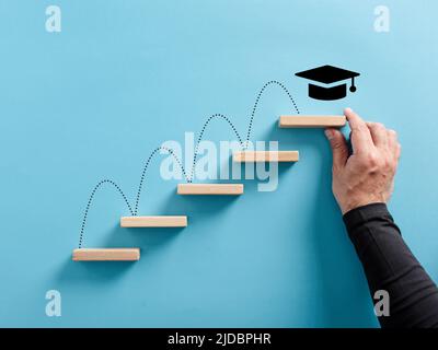 La main mâle arrange une échelle en bois avec le symbole de chapeau académique. Réalisation des diplômes et objectifs d'éducation. Banque D'Images