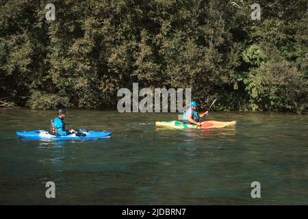 Deux kayakistes pagayant et manœuvrant sur la rivière à mouvement rapide avec une rive rocheuse et allant sous le pont de béton Banque D'Images