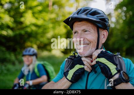 Couple senior actif à vélo au parc d'été, l'homme met sur le casque, concept de mode de vie sain. Banque D'Images