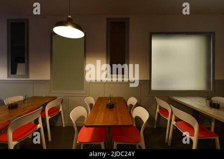 Salle à manger du restaurant avec tables rectangulaires en bois et chaises blanches avec sièges rouges Banque D'Images