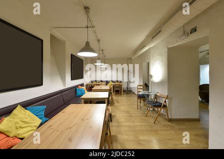 Salle à manger restaurant avec tables rectangulaires en bois naturel, fauteuil le long du mur et chaises pliantes Banque D'Images