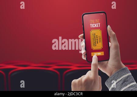 Femme tenant un smartphone et achetant des billets de cinéma en ligne à l'aide d'une application mobile, salle de cinéma et des sièges dans l'arrière-plan, POV tourné Banque D'Images