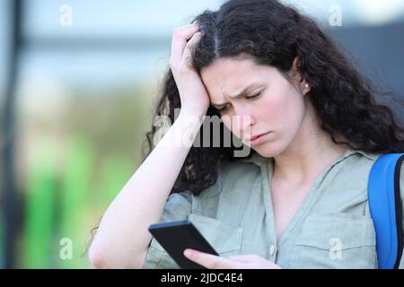 Un triste étudiant se plaint de lire un message sur un smartphone qui marche dans la rue Banque D'Images