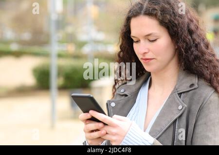 Une femme sérieuse envoie des SMS sur un téléphone portable dans la rue Banque D'Images
