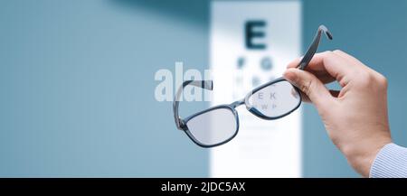 Optométriste professionnel tenant des lunettes et un graphique des yeux en arrière-plan, la vue et les problèmes de vision concept, l'espace de copie Banque D'Images