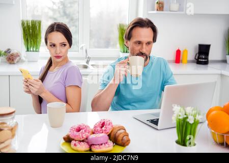 Photo de femme adulte maltraitée offensée mari habillé tenues décontractées ayant déjeuner bavardant appareils modernes à l'intérieur de la maison Banque D'Images