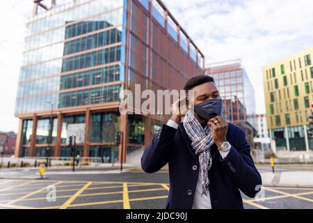 Homme debout près de la route en réglant le masque facial avec les bâtiments en arrière-plan Banque D'Images