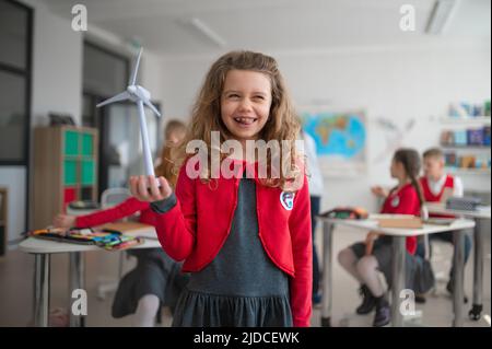 Écolière tenant une éolienne et apprenant à connaître les sources d'énergie renouvelables écologiques en classe à l'école Banque D'Images