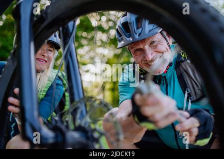 Un couple senior actif répare un vélo, pompe des pneus dans la nature en été. Banque D'Images