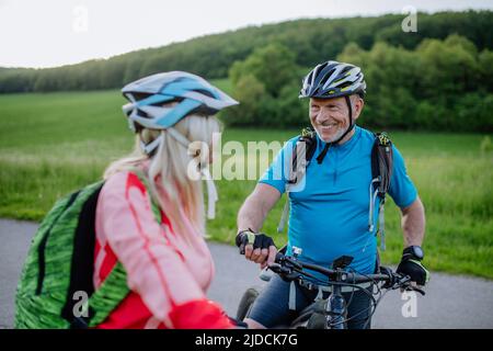 Couple senior actif à vélo électrique sur la route au parc d'été, concept de mode de vie sain. Banque D'Images