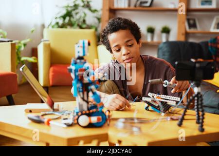 Un petit garçon instruit s'enregistrant pour un vlog et faisant un robot. Éducation en électronique et intelligence artificielle. Banque D'Images