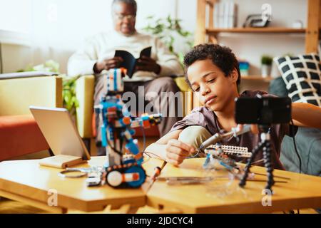 Un petit garçon instruit s'enregistrant pour un vlog et faisant un robot. Éducation en électronique et intelligence artificielle. Banque D'Images