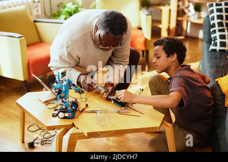 Un petit-père et un petit-fils qui font un robot ensemble à la maison. Formation en robotique et en électronique. Banque D'Images