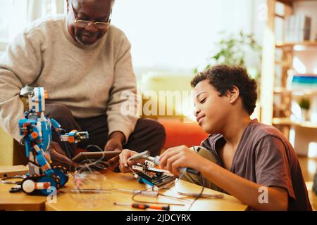 Un grand-père et son petit-enfant construisent un robot à la maison. Banque D'Images