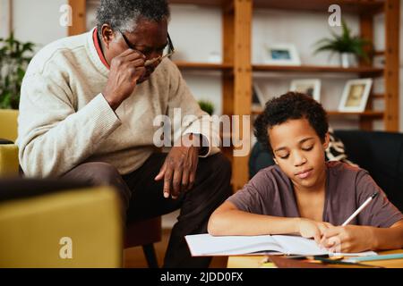 Un grand-père afro-américain est assis à la maison avec son petit-fils et l'aide pour ses devoirs. Tutorat à la maison. Banque D'Images