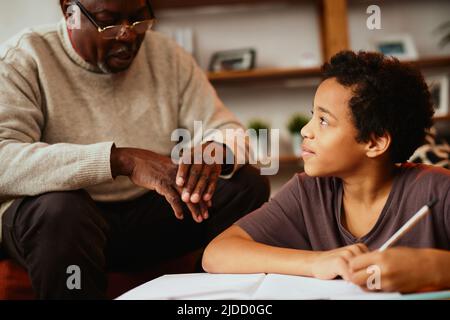 Un grand-père afro-américain est assis à la maison avec son petit-fils et l'aide pour ses devoirs. Banque D'Images