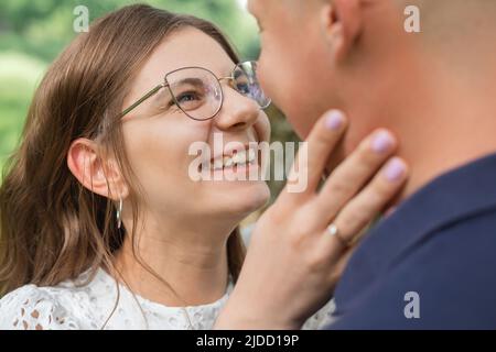 Gros plan portrait de belle femme avec des cheveux sombres dans les lunettes souriant et essayant de embrasser le petit ami dans le parc, datant Banque D'Images