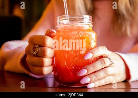 La jeune femme caucasienne tient le verre avec la poignée de la limonade aux fraises rouges avec de la glace sur une table en bois. Mains de femmes avec manucure rose et cocktail. Avant Banque D'Images