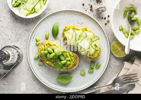 Toasts d'avocat sains avec différentes garnitures haricots edamame, concombre, basilic et graines. Vue de dessus, image en tons Banque D'Images