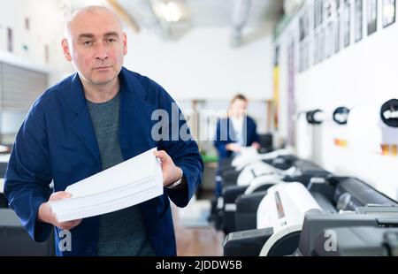 Portrait d'un employé de la maison d'impression avec pile de papier dans ses mains Banque D'Images