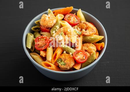 Salade de penne maison aux trois couleurs avec chapelure de crevettes, tomates et basilic dans un bol sur fond noir, vue latérale. Banque D'Images