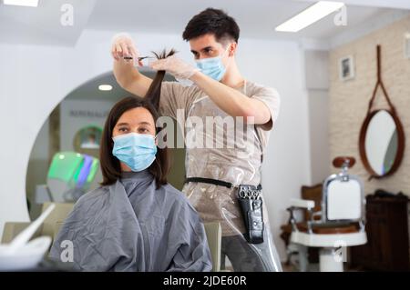 Femme cliente en masque pendant les coupes de cheveux au salon de beauté Banque D'Images