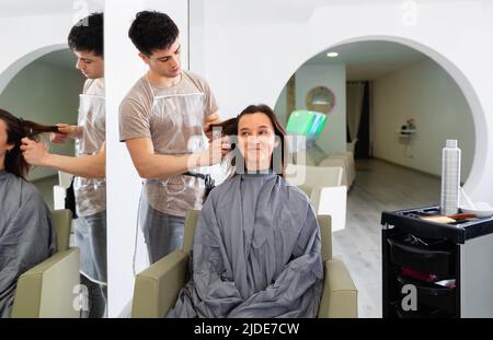 Jeune gars professionnel coiffeur coupe les cheveux de femme Banque D'Images