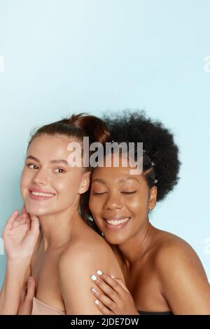 Portrait de deux merveilleuses femmes multiethniques sur fond bleu. Belles femmes, une peau impeccable. Divers amis. Banque D'Images