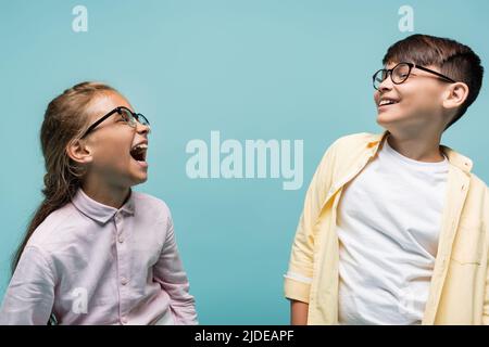 Jeunes enfants en préadolescence interraciaux souriants dans des lunettes isolées sur le bleu Banque D'Images
