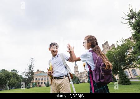 Des écoliers interraciaux souriants donnent cinq hauts dans le parc Banque D'Images