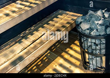 Intérieur d'un sauna finlandais avec des bancs et des pierres dans un panier en fer Banque D'Images