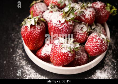 Fraises dans une assiette de sucre en poudre sur fond noir, gros plan. Banque D'Images