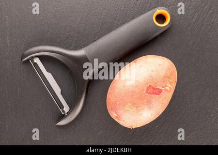 Une pomme de terre rose biologique avec un couteau sur une pierre d'ardoise, vue rapprochée du dessus. Banque D'Images