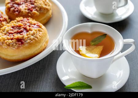 Beignets sucrés sur les assiettes et les tasses avec thé à la menthe sur la table grise. Petit déjeuner savoureux. Banque D'Images