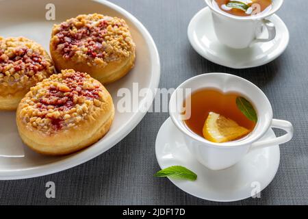 Beignets ronds doux sur les assiettes et petites tasses avec thé à la menthe sur la table. Petit déjeuner savoureux. Banque D'Images