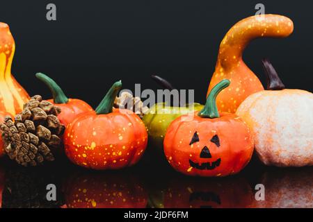 Plusieurs citrouilles de différents types, formes et couleurs, dont une citrouille d'Halloween, sur une surface réfléchissante noire, dont il y a un couple Banque D'Images