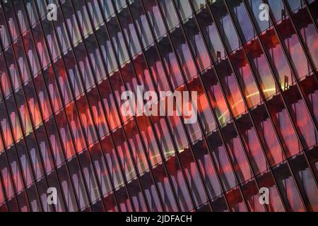 La façade en verre et en fer d'un énorme gratte-ciel au coucher du soleil, acier, couleur orange, reflet du soleil Banque D'Images