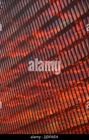 La façade en verre et en fer d'un énorme gratte-ciel au coucher du soleil, acier, couleur orange, reflet du soleil Banque D'Images