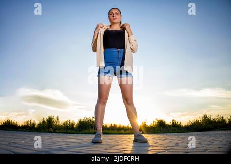 Fille en short et une chemise sur un fond de ciel clair. Banque D'Images