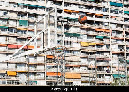 Ballon volant vers un panier avec un bâtiment résidentiel en arrière-plan, concept de sports urbains de plein air, divertissement sportif dans la ville. Banque D'Images