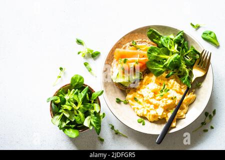 Œufs brouillés, sandwich au fromage à la crème et au saumon et feuilles de salade à la table en pierre blanche. Banque D'Images