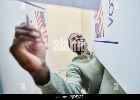 Portrait à angle bas d'un jeune homme noir mettant le bulletin de vote dans la corbeille des votes, vue de la boîte Banque D'Images