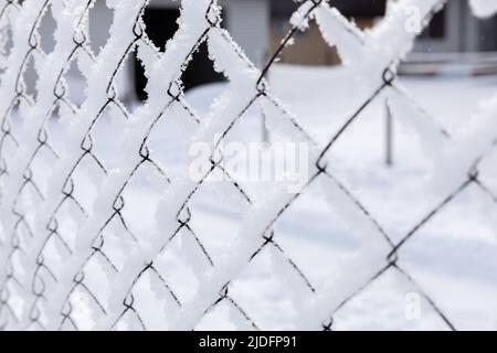 Filet de grillage glacé recouvert de neige avec un bâtiment en arrière-plan entourant les zones publiques. Exil en Sibérie. Manifestations avec les gens Banque D'Images