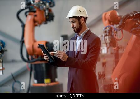 L'ingénieur en automatisation utilise une tablette pour programmer le bras robotique en usine. Banque D'Images