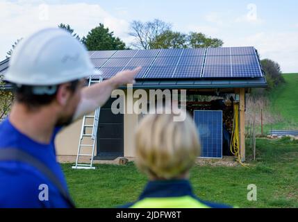 Homme et femme installateurs solaires ingénieurs avec la tablette tout en installant le système de panneau solaire sur la maison, vue arrière. Banque D'Images