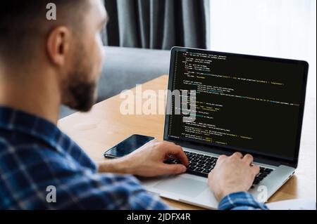 Développement de technologies de codage, concept INFORMATIQUE. Vue sur l'épaule d'un spécialiste INFORMATIQUE mâle vers un ordinateur portable avec code de programmation à l'écran. Programmateur mâle intelligent travaillant sur une nouvelle application logicielle Banque D'Images