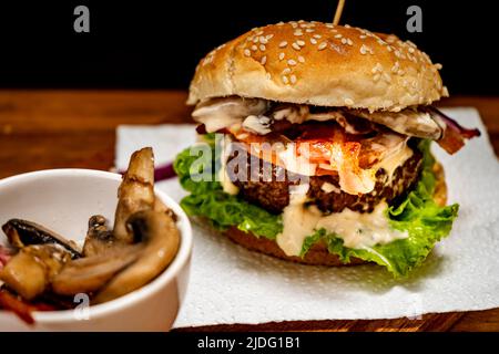 Hamburger de bœuf maison avec laitue, tomate, champignons, bacon et fromage sur une planche de bois à fond noir. Vue en morceaux. Copier le texte. Fait maison, fa Banque D'Images